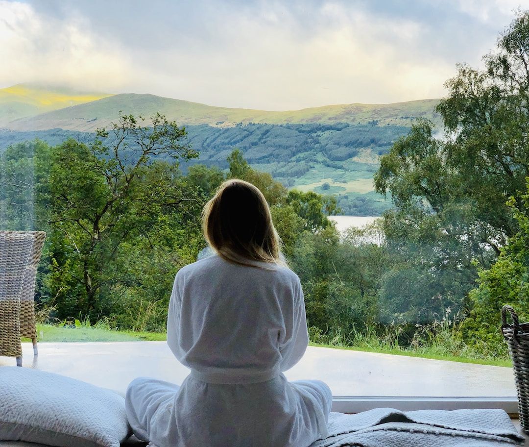 A woman in a white robe sitting quietly and looking out over green hills