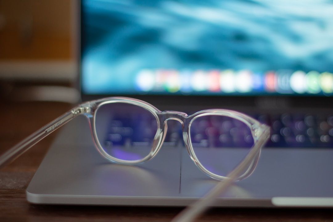 Clear glasses resting on an open laptop with a glowing blue screen