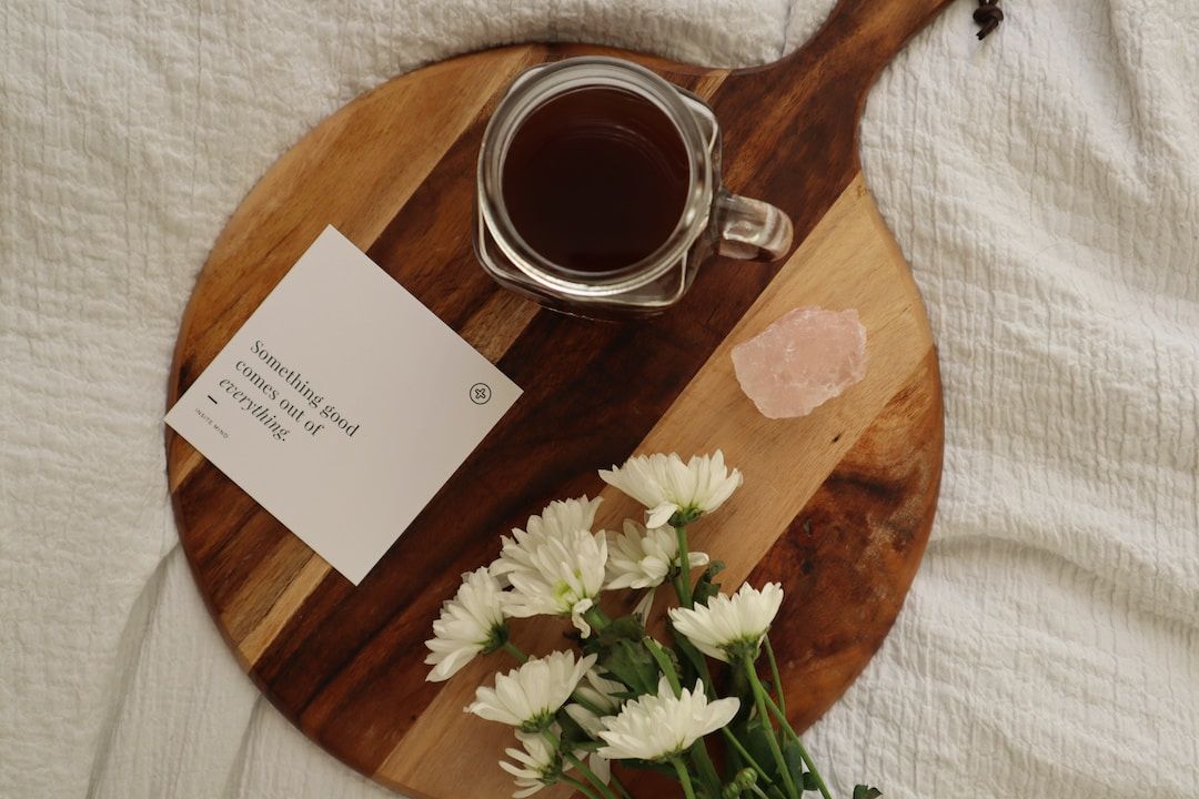 A cup of tea on a wooden board beside a handwritten note and white flowers