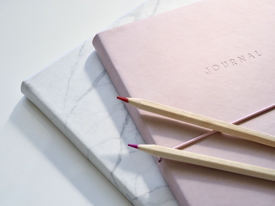 A blush pink journal and a marble notebook with colored pencils