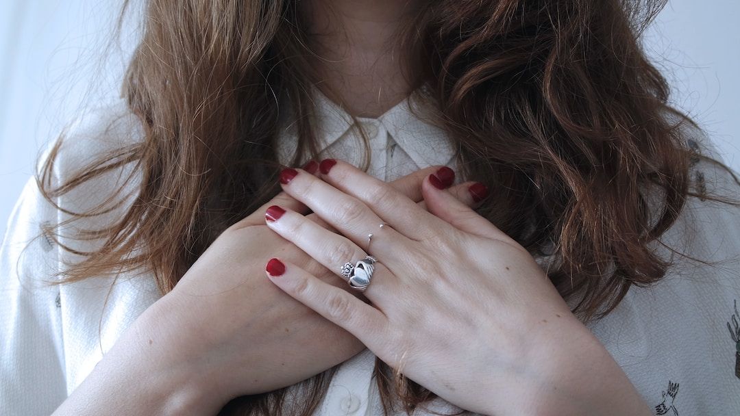 A woman with long auburn hair resting both hands over her heart