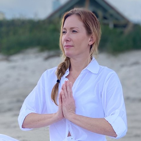 Tamara Rose meditating on the beach with her hands at her heart