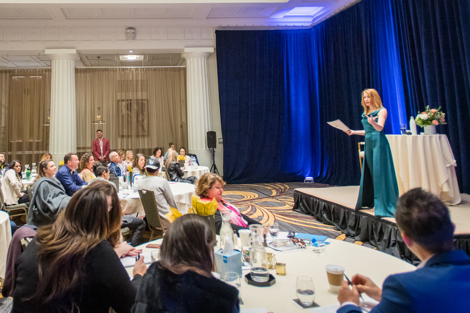 A full room of women at round tables listening as Tamara Rose teaches from the stage
