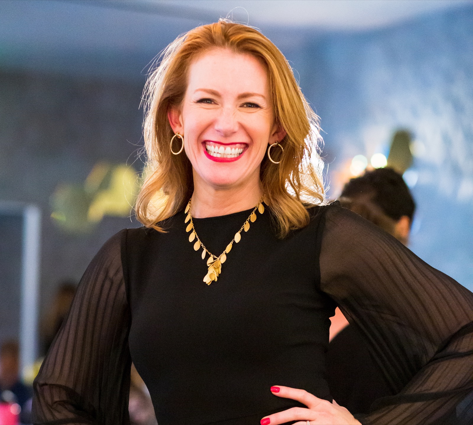 Tamara Rose smiling, hands on her hips, in a black top and gold necklace