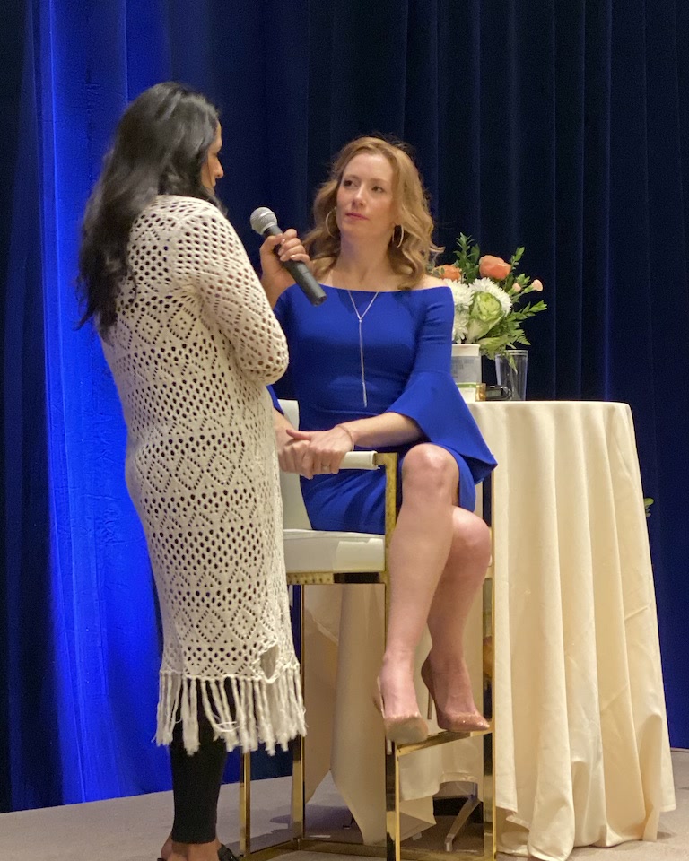 Tamara Rose in a blue dress, in a one-on-one conversation with a woman on stage