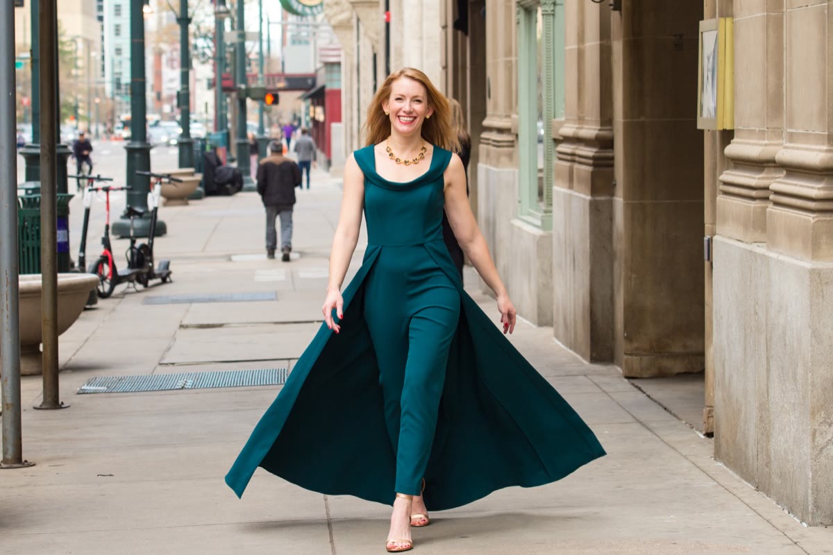 Tamara Rose walking down a city street in a flowing teal jumpsuit